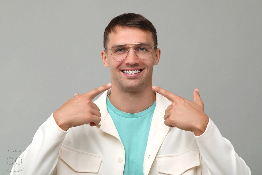 happy man pointing his metal braces grey background - Aligners vs Braces in Fairview, TN