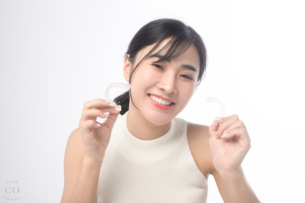 young smiling woman holding invisalign clear aligners white background studio dental - How Long Does Invisalign Take in Fairview, TN